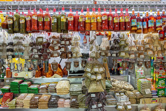 A spice and dry-goods stall in the Mercado Municipal: rows of hanging bottles of chilli and preserves above sacks and clear packets of dried herbs, beans, nuts and pulses stacked from counter to ceiling.