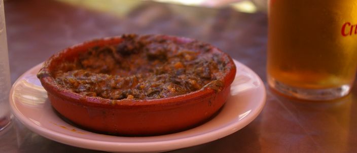 A terracotta cazuela of espinacas con garbanzos — spinach stewed with chickpeas — served as a tapa with a glass of beer.