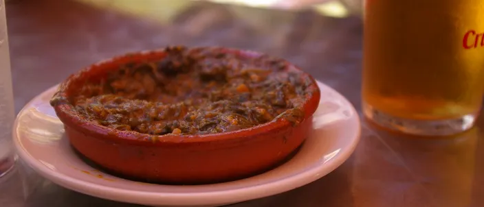 A terracotta cazuela of espinacas con garbanzos — spinach stewed with chickpeas — served as a tapa with a glass of beer.