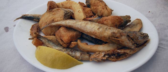 A white plate of golden-fried small whole fish with a wedge of lemon, the classic Andalusian pescaíto frito.