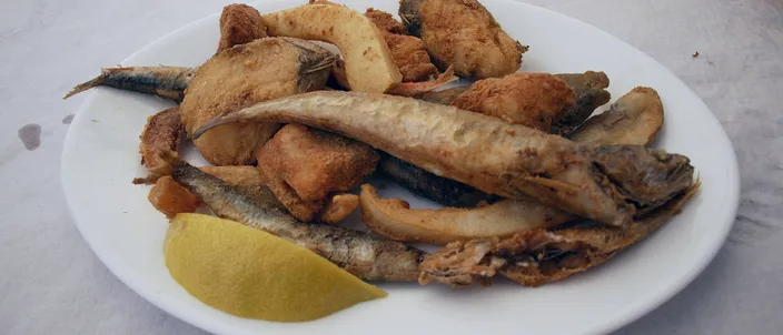 A white plate of golden-fried small whole fish with a wedge of lemon, the classic Andalusian pescaíto frito.