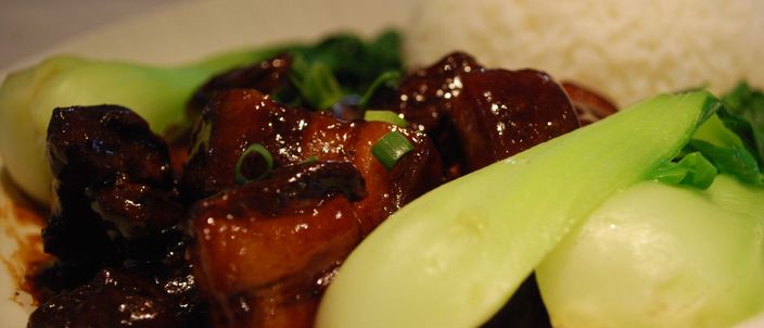 Dark, glossy cubes of red-braised pork belly in a thick mahogany glaze, served with steamed greens and a bowl of white rice.