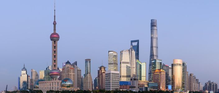 The Pudong skyline at dusk seen across the Huangpu River from the Bund — the Oriental Pearl Tower on the left, the twisting Shanghai Tower and the bottle-opener World Financial Center on the right, under a clear pale-blue sky.