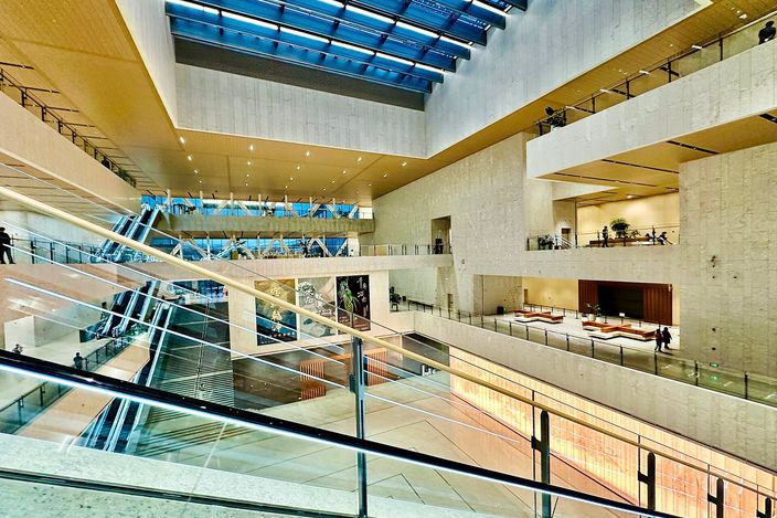 The full-height atrium of Shanghai Museum East, pale stone galleries stepping back around a skylit void six floors deep, crossing escalators on the left and visitors on the balconies.