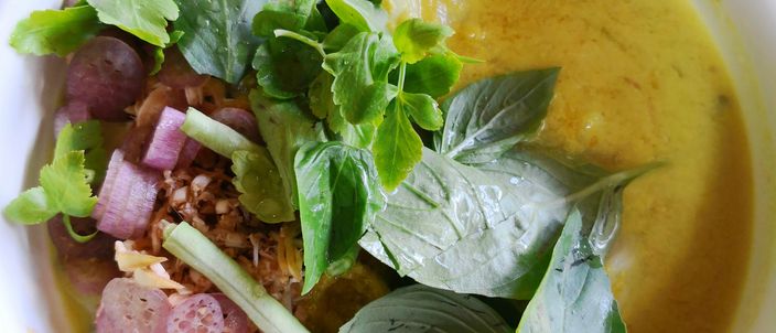 A bowl of num banh chok: rice noodles under a yellow fish-and-lemongrass gravy, topped with fresh herbs, bean sprouts and banana blossom.