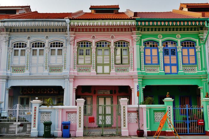 Three Peranakan shophouses on Koon Seng Road in white, pink and green, their upper windows framed by moulded plaster garlands and glazed tiles, low swing gates across the front doorways