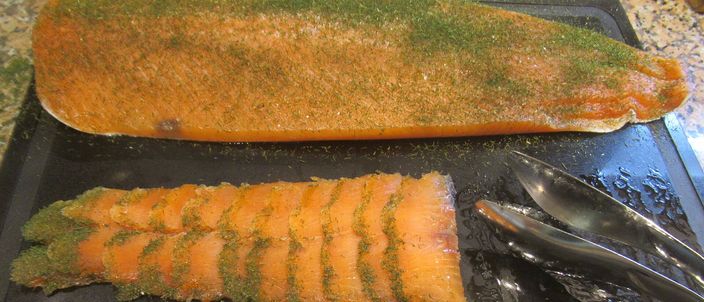 A whole side of cured salmon topped with a layer of chopped dill, with translucent thin slices cut from it laid alongside.