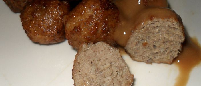 A plate of small Swedish meatballs in a pale cream gravy, one meatball cut open to show the tender interior.
