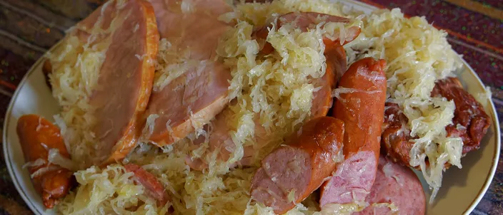 A plate of choucroute garnie: pale sauerkraut heaped with sliced ham, smoked sausages and pork