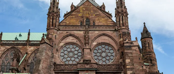 The south transept of Strasbourg Cathedral in pink sandstone, its two rose windows above the painted dial of the exterior clock