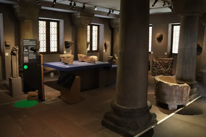 A room of the Musée de l'Œuvre Notre-Dame, stone columns and medieval sculpture fragments under low lights