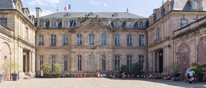 The cobbled courtyard of the Palais Rohan, its pale sandstone wings closing round the square under a blue sky