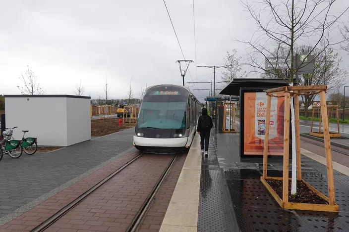 A Strasbourg tram pulling into a stop with a shelter and a row of rental bicycles beside the platform