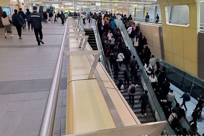 Crowds of commuters riding escalators and walking through a busy MRT station concourse in Taipei, with overhead departure signage and a curved gold ceiling.