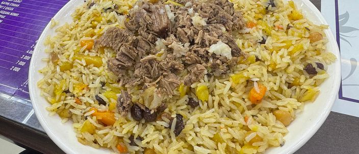 A platter of Tashkent wedding plov: glossy amber rice with julienned carrots, topped with pieces of braised meat and raisins.