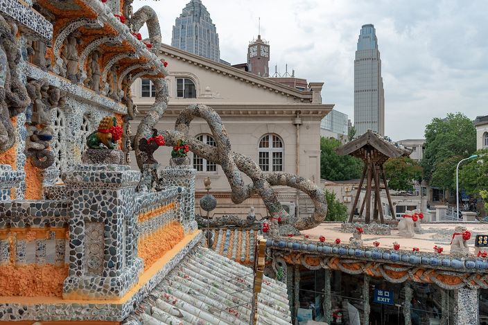 The roof and eaves of the Porcelain House, encrusted with broken blue-and-white china, orange tilework and small stone dragons, with modern office towers rising behind it.