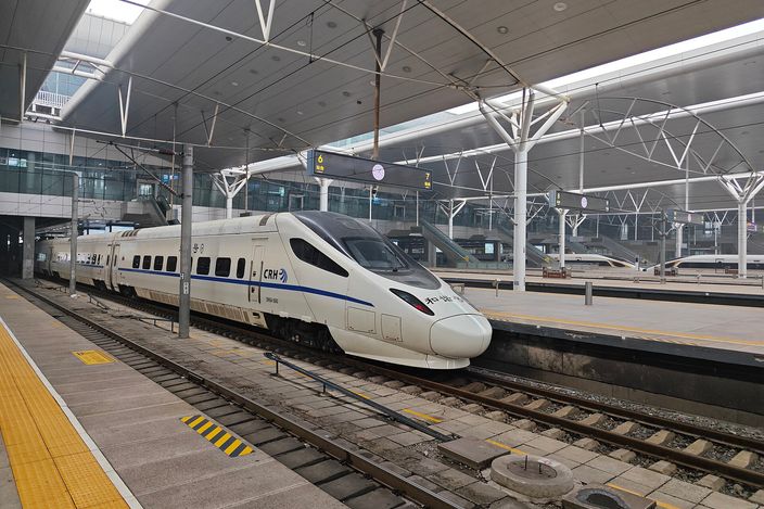 A white CRH high-speed train standing at a platform beneath the steel canopy of Tianjin Railway Station, its nose towards the camera, with further trains at the platforms behind.