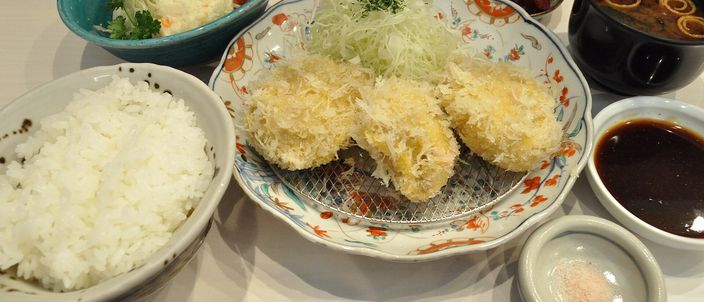 A tonkatsu teishoku on a lacquer tray: shaggy golden cutlets on an ornate plate with a mound of shredded cabbage, bowls of rice and soup, pickles, dipping sauce and a dish of pink salt.