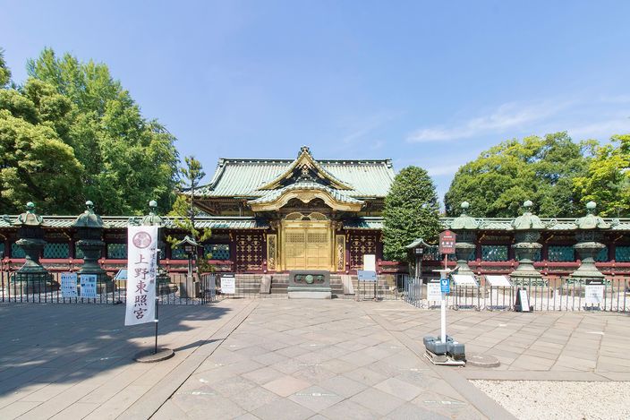 Ueno Tosho-gu: the small gold-leafed shrine hall at the end of its forecourt, rows of bronze lanterns lined up behind the fence on either side, trees closing in around it