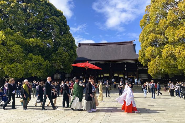 The courtyard of Meiji Jingū with visitors crossing it and a Shinto wedding procession under the shrine's wooden eaves