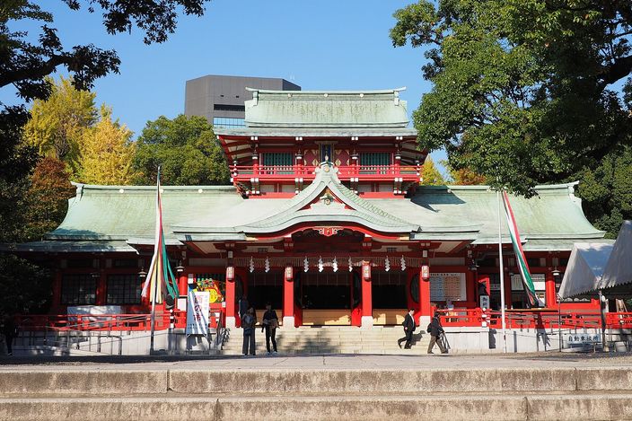 Tomioka Hachiman Shrine's vermilion and white hall at the top of its steps, with visitors crossing the forecourt