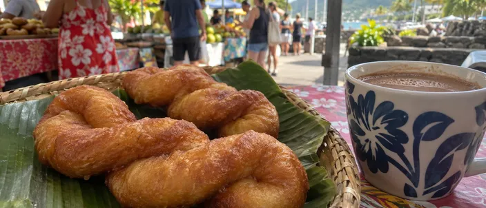 AI-generated image of firi firi: golden figure-of-eight doughnuts on a banana leaf in a woven basket at a market stall, a cup of hot chocolate beside them.