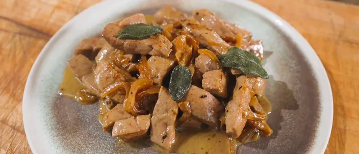 A plate of fegato alla veneziana: pale strips of calf's liver mixed with soft-cooked onions and their pan juices, finished with a few sage leaves.