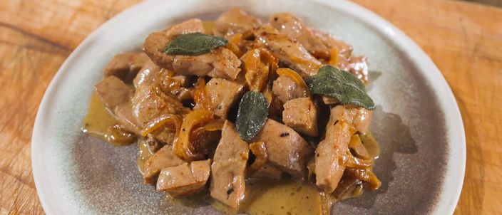 A plate of fegato alla veneziana: pale strips of calf's liver mixed with soft-cooked onions and their pan juices, finished with a few sage leaves.