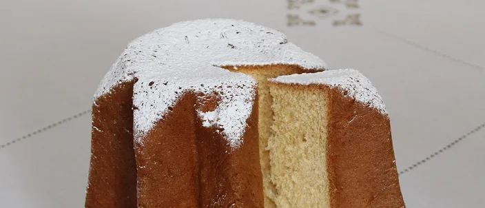 A whole pandoro cake sliced open to reveal its pale golden, eight-pointed star cross-section, dusted with powdered sugar and set on a glass plate.