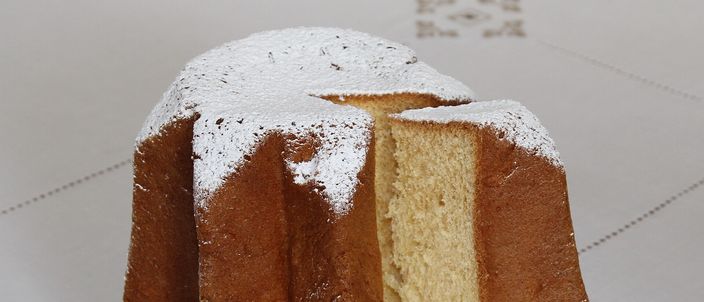 A whole pandoro cake sliced open to reveal its pale golden, eight-pointed star cross-section, dusted with powdered sugar and set on a glass plate.