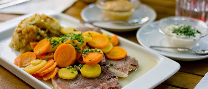 A plate of sliced Wiener Tafelspitz boiled beef with rounds of carrot and potato and a sauce, on a white plate in a Viennese tavern