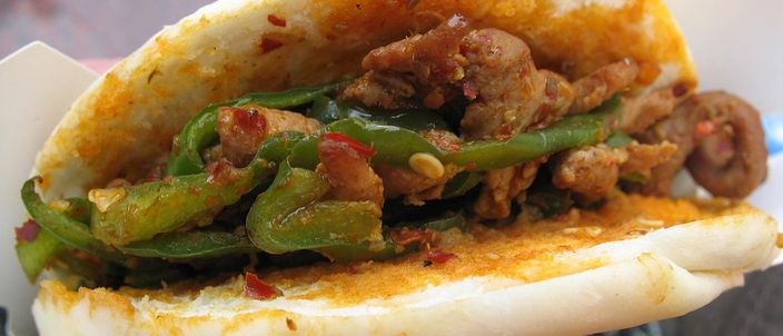 A roujiamo held in a paper wrapper: a griddled flatbread split open around chopped braised meat mixed with sliced green chillies.