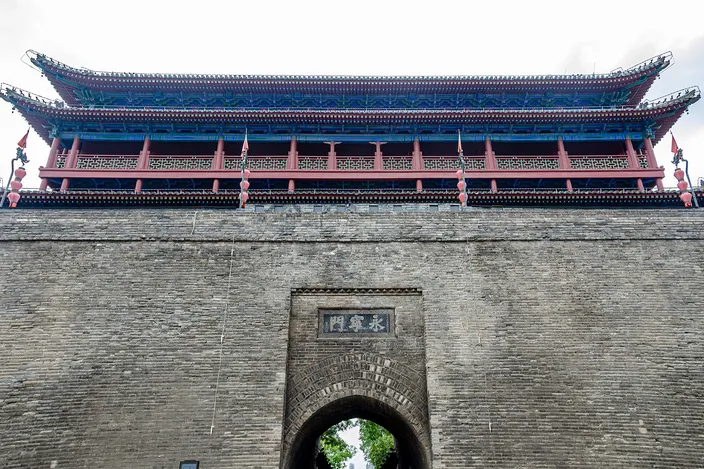 The double-eaved gate tower of Yongningmen rising above the gray brick city wall, seen from street level with the archway below.
