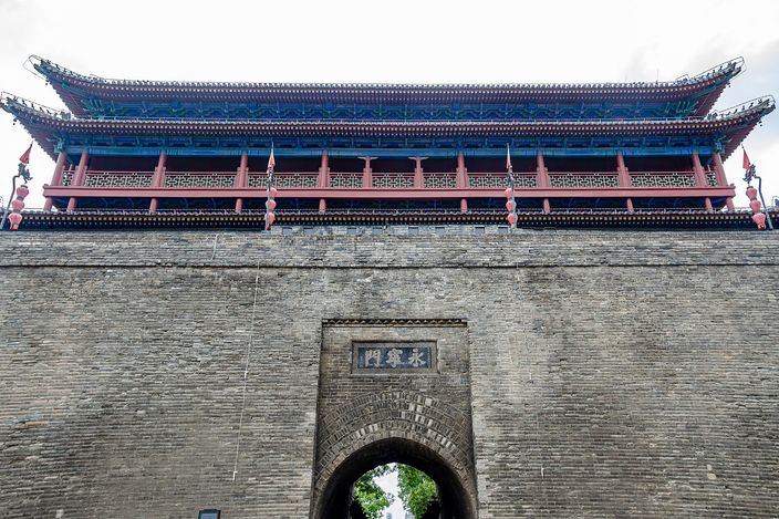 The double-eaved gate tower of Yongningmen rising above the grey brick city wall, seen from street level with the archway below.