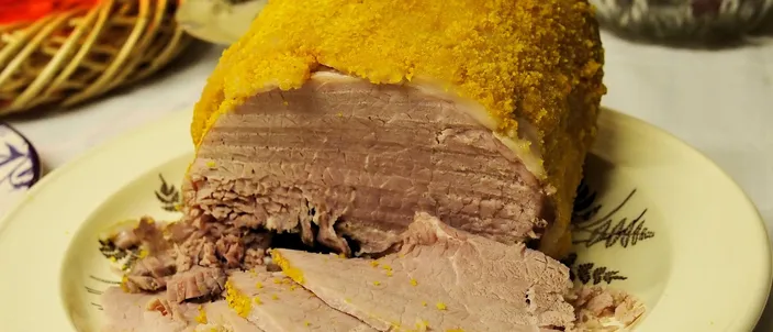A cooked York ham with a golden breadcrumb coat, cut open on a cream plate to show pale pink, close-grained slices