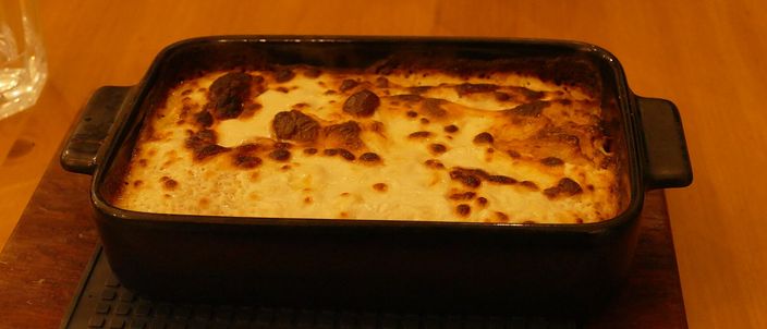 A baked portion of štrukli in a dark rectangular dish, its cheese-and-cream topping browned and blistered.