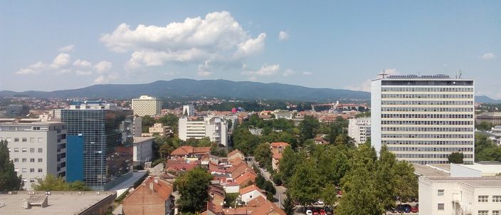 Zagreb rooftops from the Eurotower: red-tiled houses and mid-rise blocks stretching to Medvednica mountain under a blue summer sky
